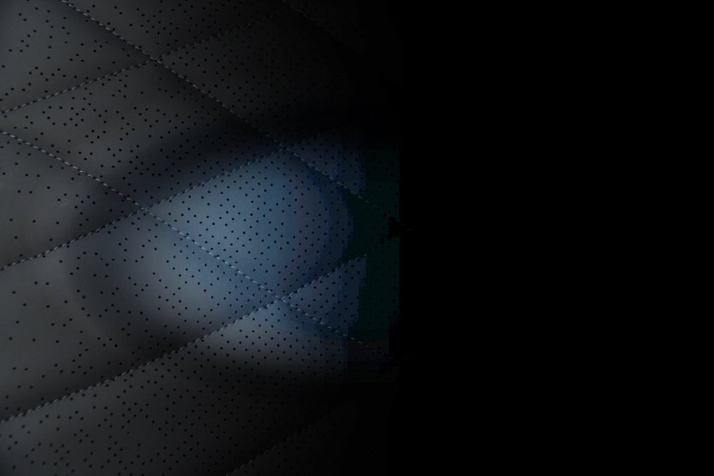 Close-up of a quilted, perforated surface partially illuminated, with the rest fading into darkness on the right side of the image.