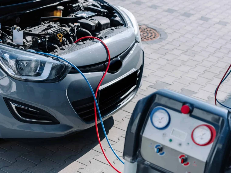A car with its hood open is connected to an air conditioning service machine using red and blue hoses, showcasing professional Air Conditioning Services in an outdoor setting.