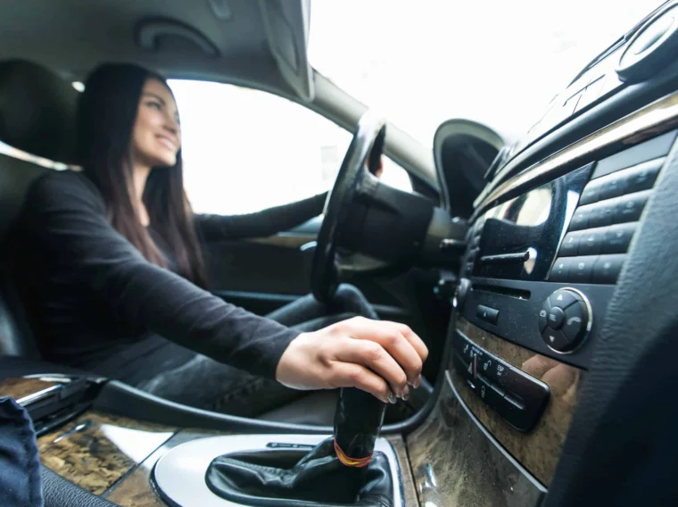 Person sitting in the driver’s seat of a car, one hand on the steering wheel and the other shifting the gear lever, possibly after a recent clutch replacement.