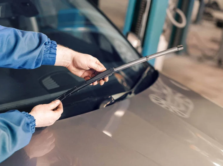 Person in a blue jacket performing wiper replacement on a car’s windshield.