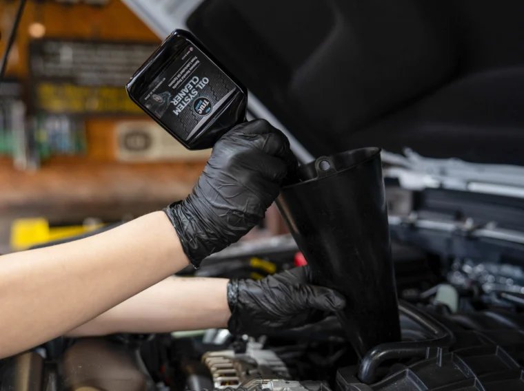 A person wearing black gloves pours engine oil through a funnel into a car’s engine compartment, performing essential engine maintenance to keep the vehicle running smoothly.