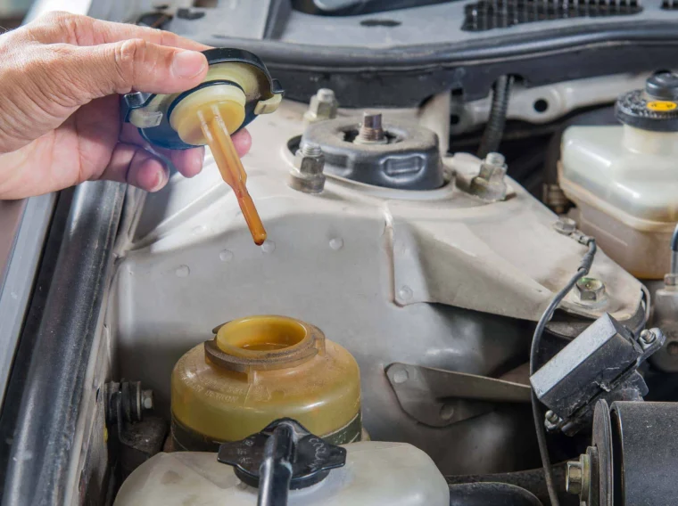 A hand holds a brake fluid reservoir cap with a dipstick above an open brake fluid reservoir in a car engine bay, highlighting the importance of regular maintenance alongside power steering and other essential steering services.