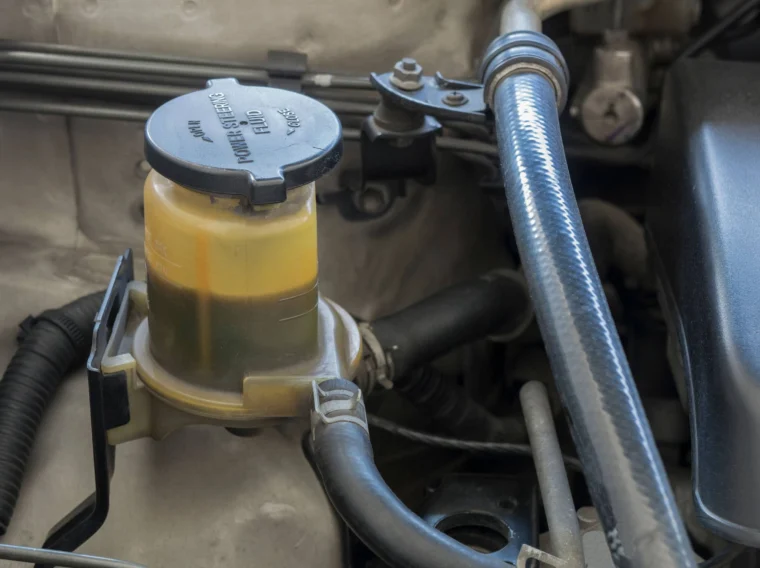 A close-up view of a vehicle's brake fluid reservoir, showing fluid with visible discoloration, is seen under the hood—an important detail during routine power steering and steering services.
