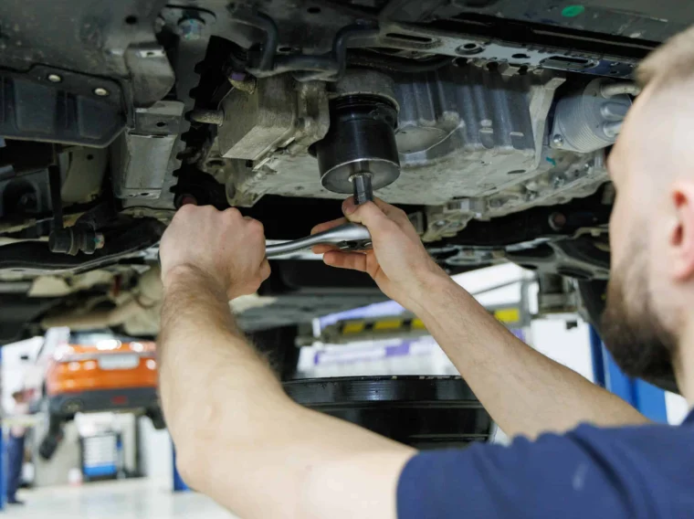 A mechanic uses a wrench to work on the underside of a vehicle in an auto repair shop.