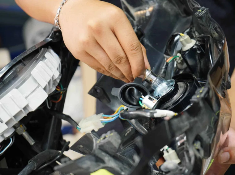 A person installs a headlight bulb into a vehicle headlight housing, with visible wires and connectors, as part of routine Headlight Services.