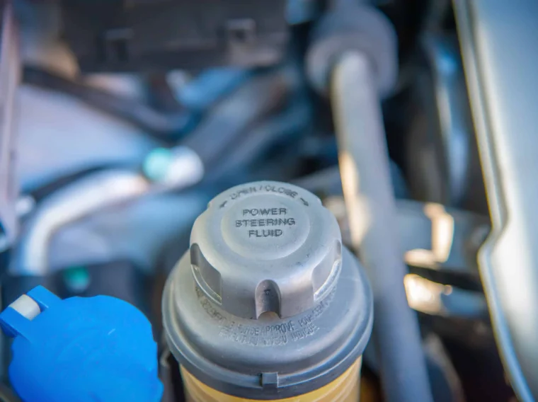 Close-up of a power steering fluid reservoir cap in a car engine bay, highlighting "Power Steering Fluid" and instructions for opening—essential for proper Power Steering performance and regular Steering Services.