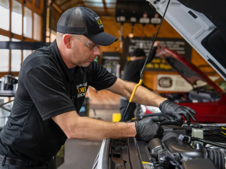 A mechanic wearing gloves and safety glasses works under the hood of a vehicle in a garage, providing preventive maintenance services to ensure optimal performance.