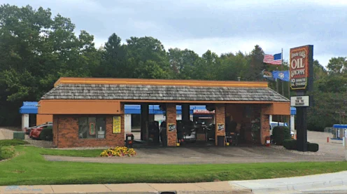 A single-story oil change shop with three open service bays, a sign reading “10 Minute Oil Change,” and cars parked inside and outside. Trees and other buildings are in the background.