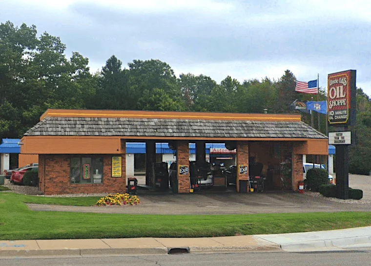 A single-story oil change shop with three open service bays, a sign reading “10 Minute Oil Change,” and cars parked inside and outside. Trees and other buildings are in the background.