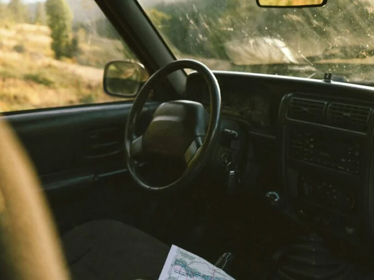 A car interior with a steering wheel, dashboard, and a map on the seat; through the window, the blurred outdoor landscape hints at adventure—truly one of those Cars of Character.