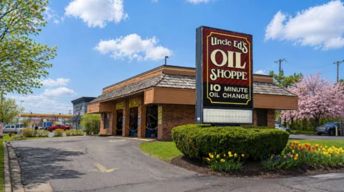 A single-story brick building with a large sign reading "Uncle Ed's Oil Shoppe 10 Minute Oil Change" in front, surrounded by flowers and a paved driveway.